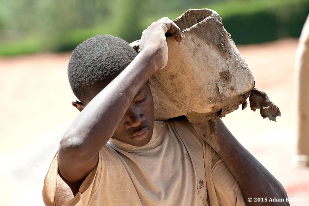 portland oregon editorial photographer in rwanda -man carrying bucket of cement